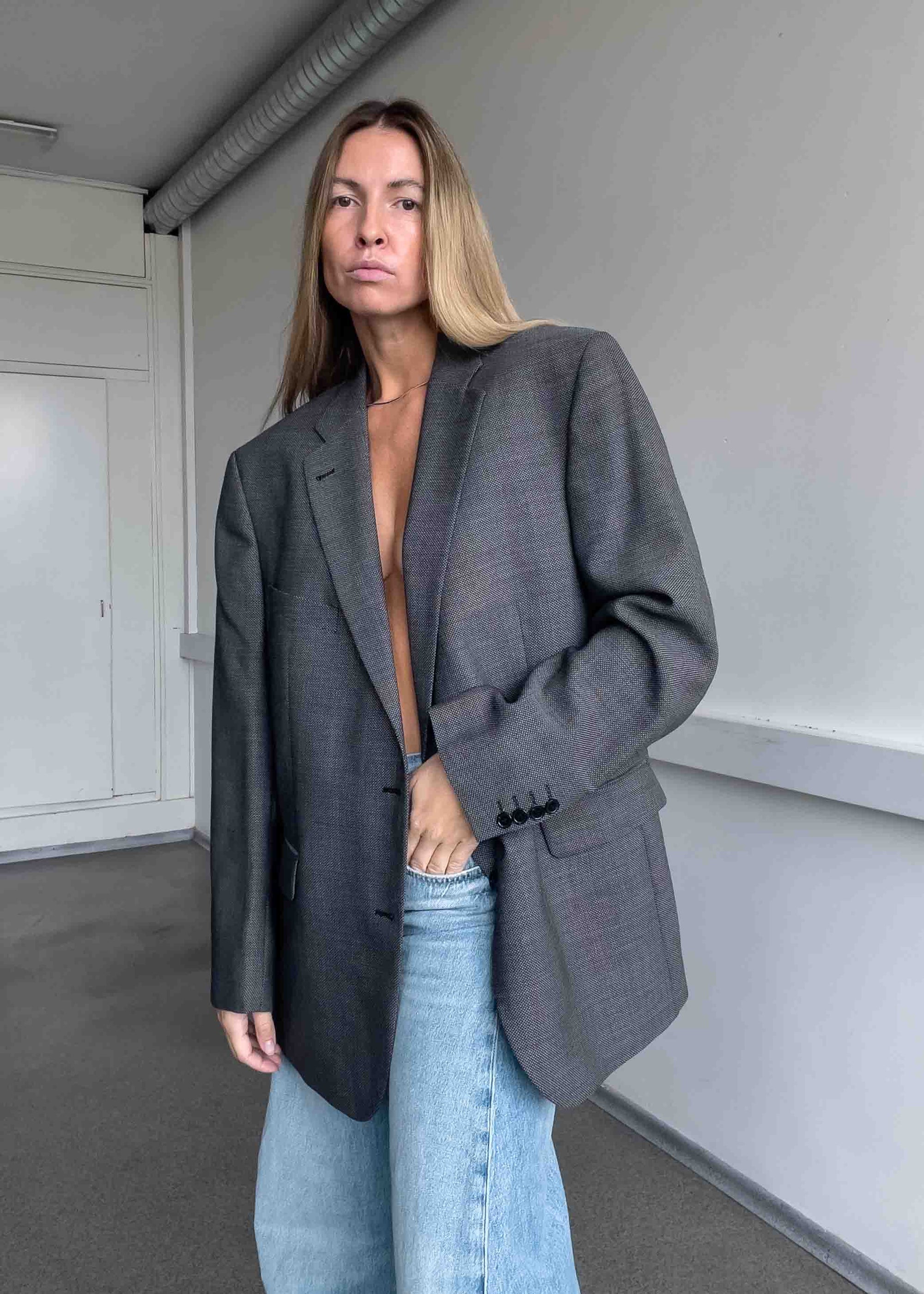 Person wearing a gray blazer over a black top with light blue jeans in an indoor setting.